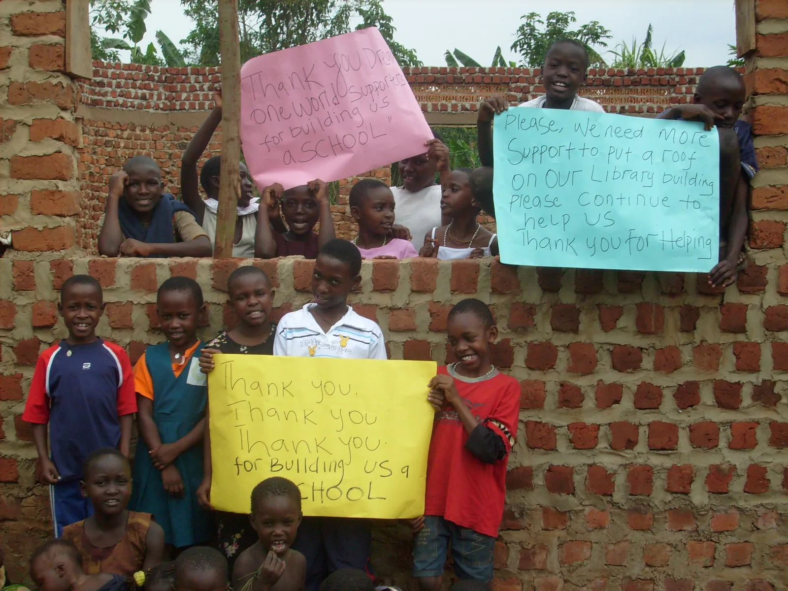 Children holding handwritten signs among the brick walls of a school building under construction