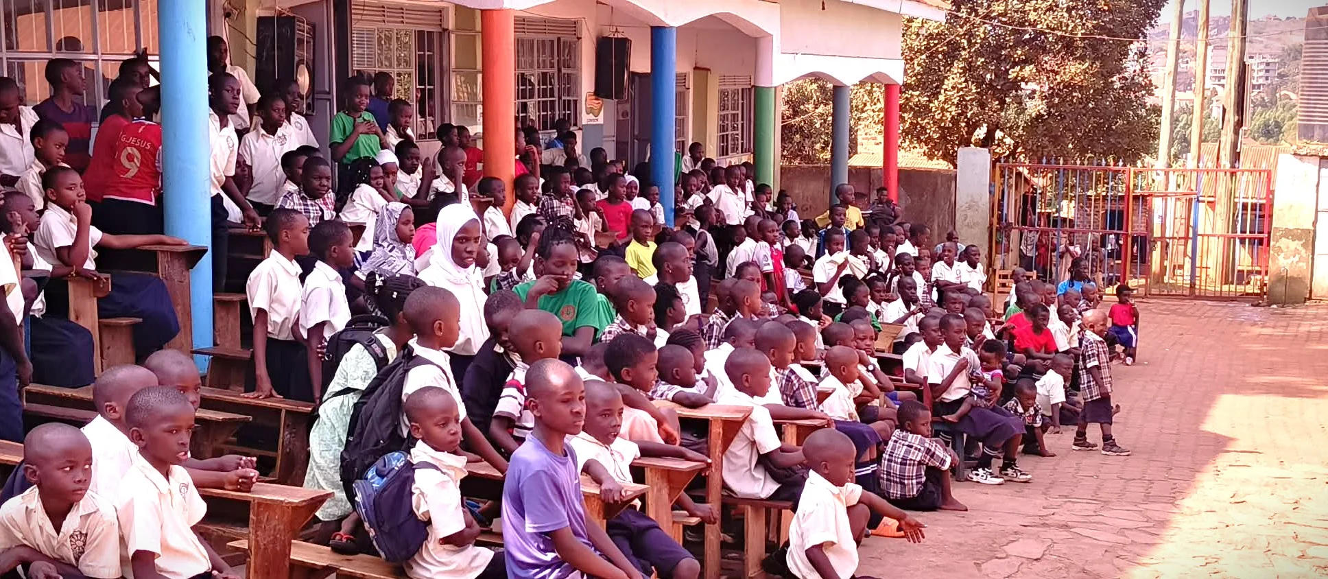 Children gathered on benches and in the courtyard at Uganda Dream School