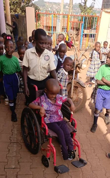 An older student helping a younger child in a wheelchair through the schoolyard